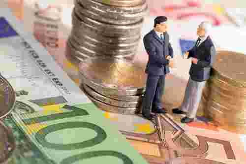 Foto: Zwei kleine Figuren stehend auf Geldscheine umringt von Münzen 